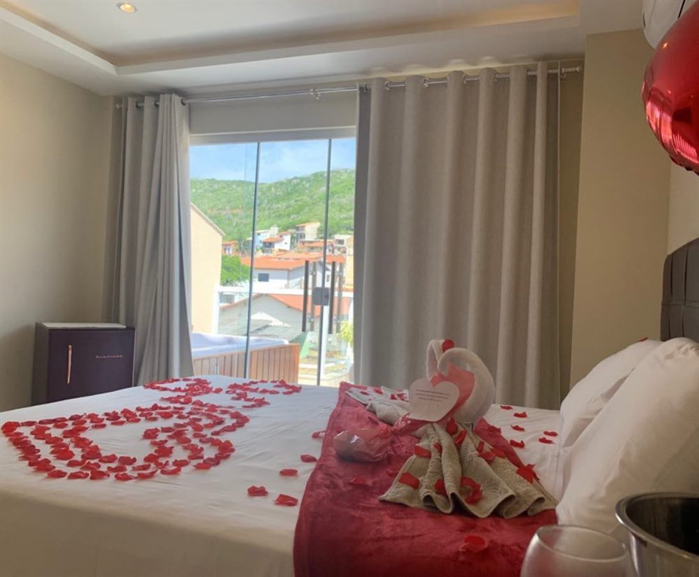 Quarto com pétalas de rosa na cama, toalha em forma de cisne e balão de coração